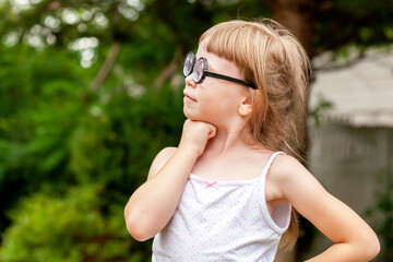 One little smart clever young school age girl, happy child wearing big quirky glasses standing proud, thinking deep in thought pose outdoors portrait, copy space. Children lifestyle, education concept