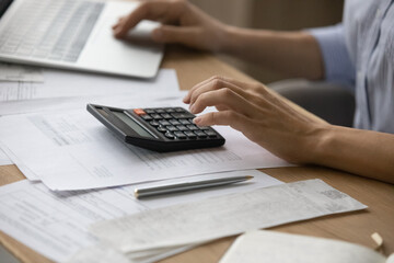 Close up cropped of woman calculating and paying bills, using laptop and calculator, young female...