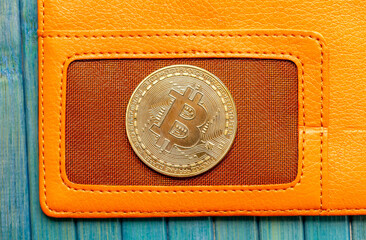 One single bitcoin gold coin symbol laying on a stylish trendy orange wallet top view, macro, extreme closeup, shot from above. Business, finance, BTC cryptocurrency simple abstract concept, nobody