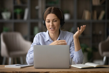 Smiling businesswoman in headset using laptop, consulting client online or negotiating with...