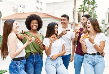 Group of young friends smiling happy eating pizza standing at the city.