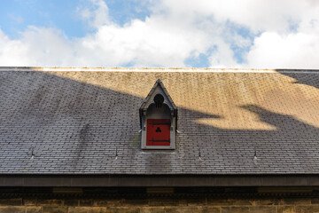 Exterior view of ornamental gabled dormer on old rough roof of church in Europe. 