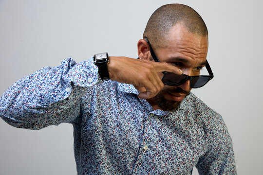 Cool Latino man with black sunglasses lowered looks attentively at the copy space on a white background