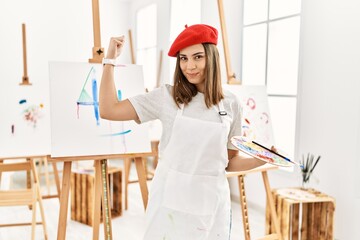 Young artist woman painting on a canvas at art studio strong person showing arm muscle, confident and proud of power