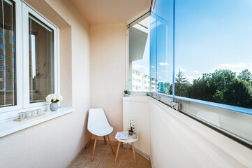 Small balcony on one of upper floors of apartment building. There is chair with coffee table of the same design. Balcony is then complemented by small decorative items. There is also glass protection.