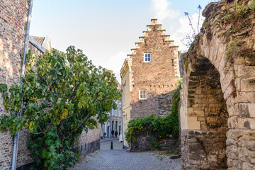 Fototapeta na wymiar Outdoor scenery of narrow alley along Jeker canal and ruin historical city wall in Autumn season, in Maastricht, Netherlands during evening sunset time.