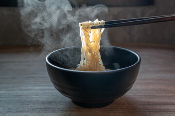 Lift with wood chopsticks  to pickup noodle with steam and smoke  on black background. korea,...