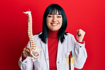 Young hispanic doctor woman holding anatomical model of spinal column screaming proud, celebrating victory and success very excited with raised arm