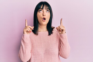 Young hispanic woman wearing casual clothes amazed and surprised looking up and pointing with fingers and raised arms.