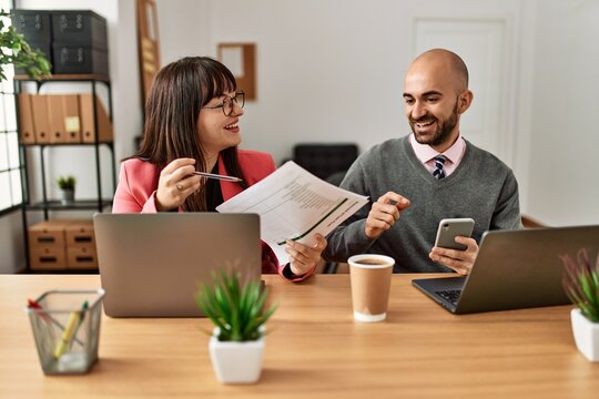Two hispanic business workers smiling happy working using laptop and smartphone at the office.
