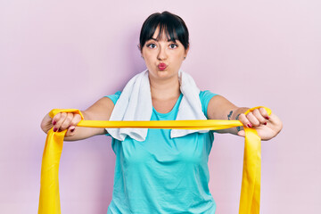 Young hispanic woman wearing sportswear and arm band puffing cheeks with funny face. mouth inflated with air, catching air.