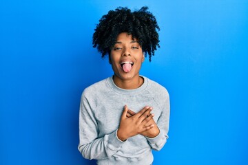 African american woman with afro hair wearing sportswear doing heart symbol with hands sticking tongue out happy with funny expression.