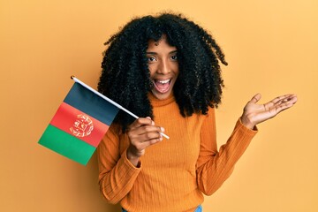 African american woman with afro hair holding afghanistan flag celebrating achievement with happy smile and winner expression with raised hand