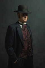 Young man in stylish vintage Victorian attire stands in a room in front of a dark gray wall.