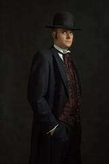 Young man in stylish vintage Victorian attire stands in a room in front of a dark gray wall.