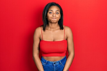 Young african american girl wearing casual style with sleeveless shirt puffing cheeks with funny...