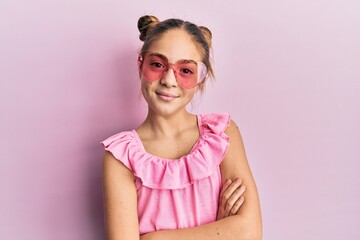Beautiful brunette little girl wearing heart shaped sunglasses happy face smiling with crossed arms looking at the camera. positive person.
