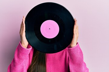 Woman holding retro vinyl disc covering face over pink background