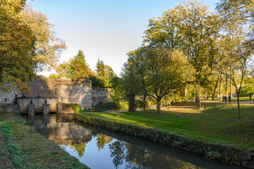 Outdoor scenery of walking way along Jeker canal and historical city wall at Monseigneur Nolenspark, city public park, in Autumn season, in Maastricht, Netherlands during evening sunset time.
