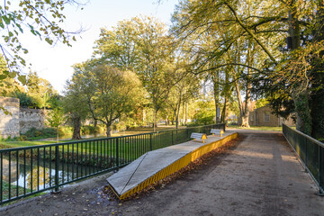 Outdoor scenery of walking way along Jeker canal and historical city wall at Monseigneur Nolenspark, city public park, in Autumn season, in Maastricht, Netherlands during evening sunset time.
