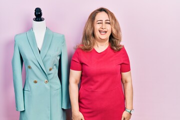 Middle age caucasian woman standing by manikin winking looking at the camera with sexy expression,...