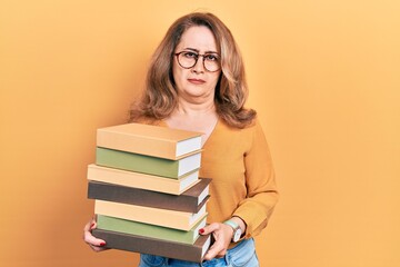 Middle age caucasian woman holding a pile of books skeptic and nervous, frowning upset because of problem. negative person.