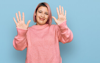 Hispanic woman with pink hair wearing casual winter sweater showing and pointing up with fingers number ten while smiling confident and happy.