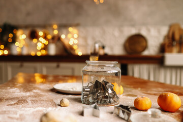 A glass jar with cookie molds stands on a wooden table on a Christmas holiday in a decorated loft style kitchen in a cozy house, a selective focus