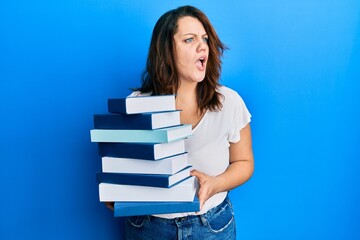 Young caucasian woman holding a pile of books angry and mad screaming frustrated and furious, shouting with anger. rage and aggressive concept.