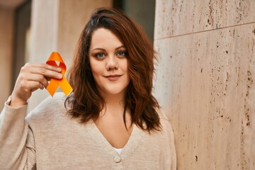 Young irish plus size girl smiling happy holding orange awareness ribbon at the city.