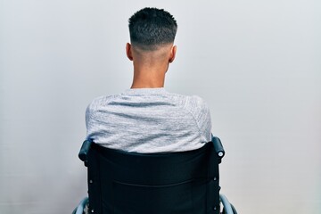 Young hispanic man sitting on wheelchair standing backwards looking away with crossed arms