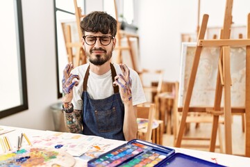 Hispanic man with beard at art studio gesturing finger crossed smiling with hope and eyes closed. luck and superstitious concept.