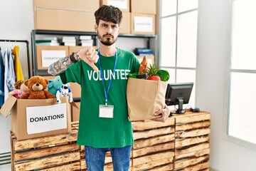 Hispanic man with beard wearing volunteer t shirt at donations point with angry face, negative sign...