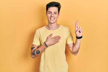 Young hispanic man wearing casual yellow t shirt smiling swearing with hand on chest and fingers...