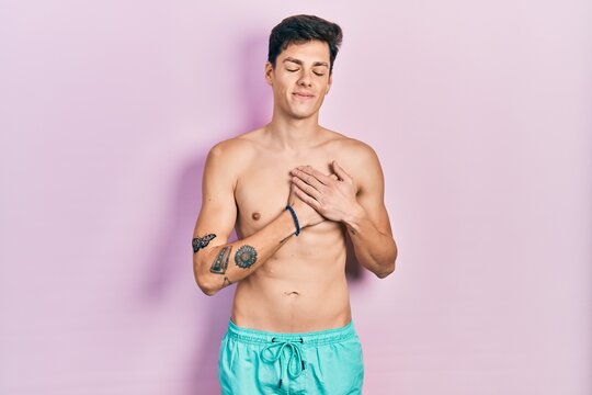 Young hispanic man wearing swimwear shirtless smiling with hands on chest with closed eyes and grateful gesture on face. health concept.