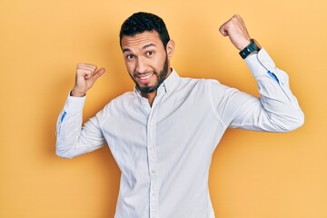 Hispanic man with beard wearing business shirt showing arms muscles smiling proud. fitness concept.