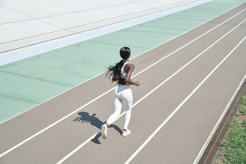 Top view of beautiful young African woman in sports clothing running on track outdoors
