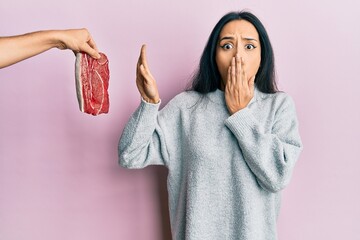 Young hispanic girl on diet rejecting beef covering mouth with hand, shocked and afraid for...