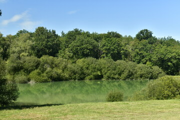 L'étang aux eaux émeraudes entre forêt et prairie sous un ciel d'été près du Bourg de...