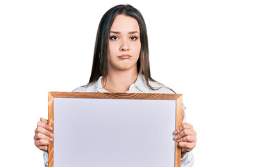 Young hispanic woman holding empty white chalkboard depressed and worry for distress, crying angry and afraid. sad expression.