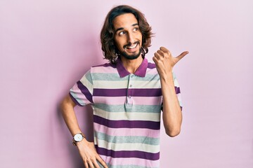 Young hispanic man wearing casual clothes pointing thumb up to the side smiling happy with open mouth