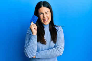 Beautiful brunette woman holding credit card winking looking at the camera with sexy expression,...