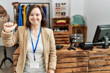 Young down syndrome woman working as manager at retail boutique showing and pointing up with finger number one while smiling confident and happy.