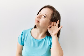 Fototapeta premium Young down syndrome woman standing over isolated background smiling with hand over ear listening an hearing to rumor or gossip. deafness concept.