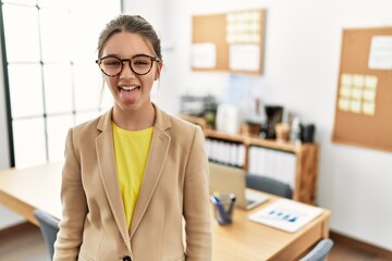 Young brunette teenager wearing business style at office sticking tongue out happy with funny expression. emotion concept.