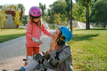 Little cute girl helping her grandmother wearing helmet prepairing for roller skating