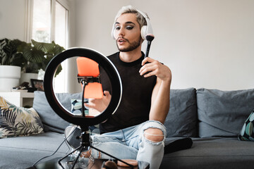 Gay man streaming online make up video tutorial with mobile phone indoors at home - Lgbt, drag queen, technology trendy concept - Focus in face - obrazy, fototapety, plakaty