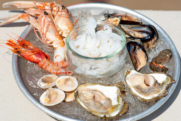 Plate of raw fresh sea fruit or food, ready to eat with prawns, shrimps, oysters, mussels, shells, cuttlefish, close up