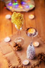 Christmas decorations in rustic style. Christmas beads in champagne glasses. Pine cones and burning candles on sackcloth on Christmas Eve. Festive concept