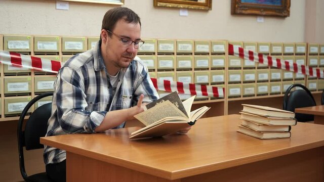 man reading a book while sitting at a table in the library